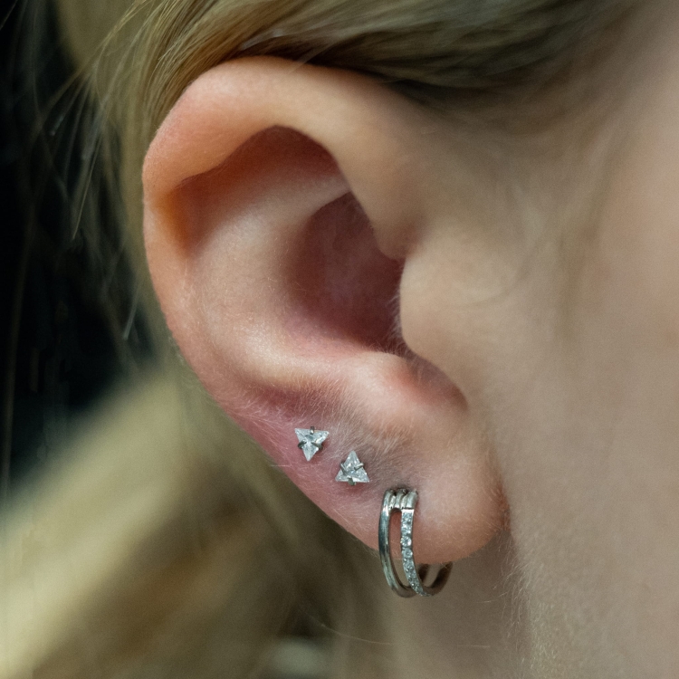 Kryształowy trójkąt w szponach - tytanowy ozdobny labret. Kolczyk kryształ do piercingu ucha - lobe, tragus, forward helix, conch, flat. Biały w uchu, podwójne przekłucie upper lobe.